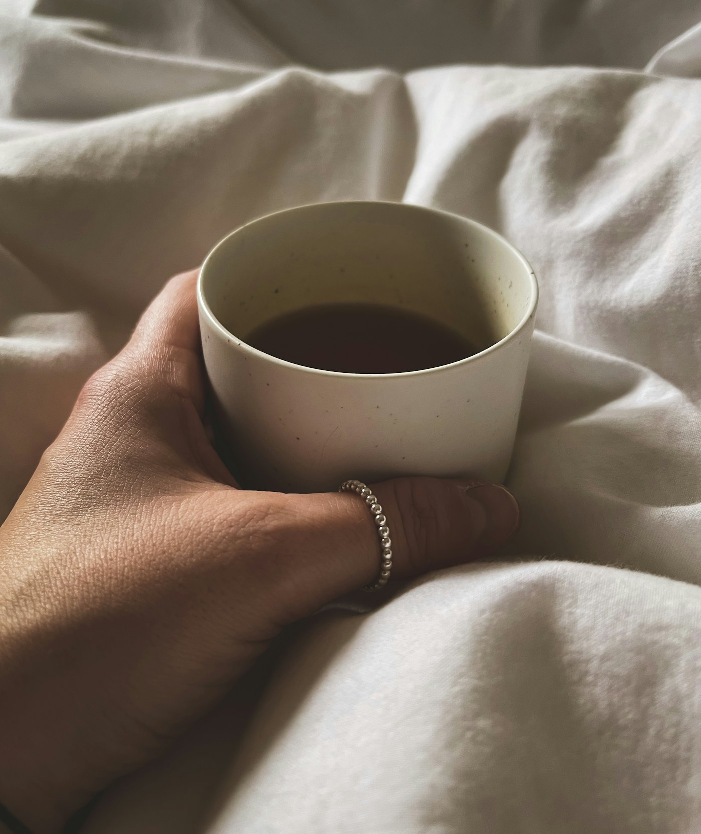 A hand holding a warm mug of ginger tea resting on soft bedding in morning light.